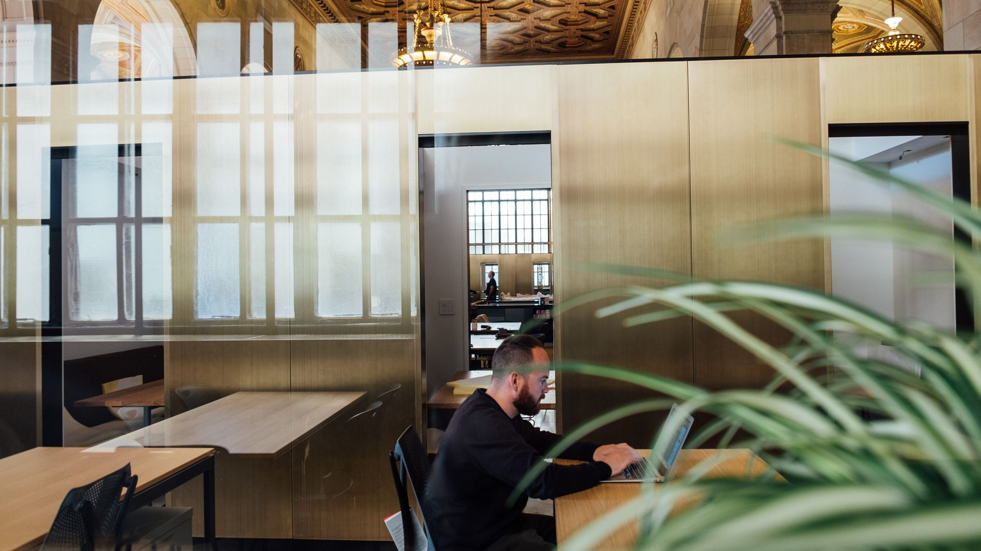 A quiet open office: long desks, glass walls, one person at work