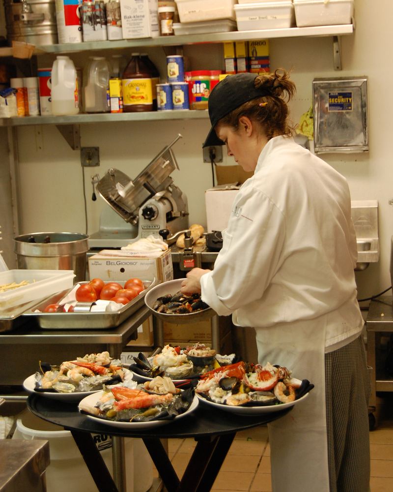 A cook plating seafood on the pass in a small, busy kitchen