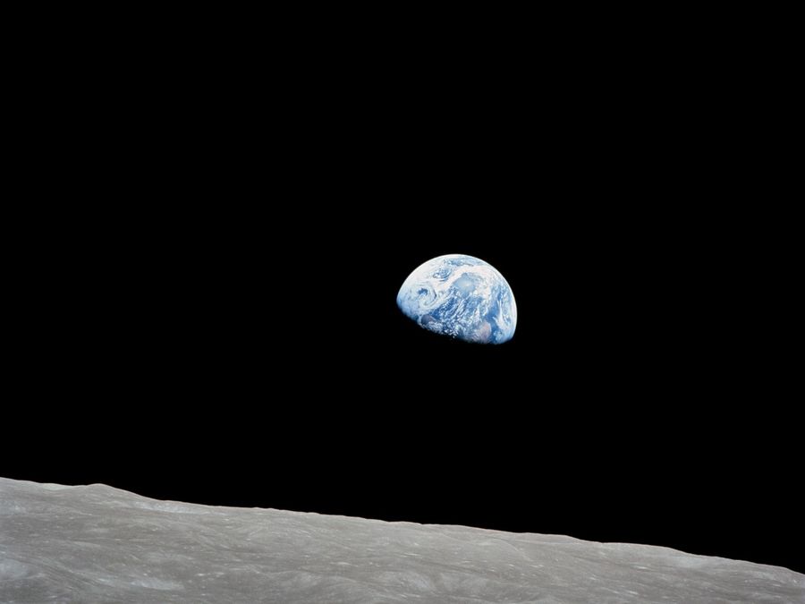 The Earth, half lit, rising over the gray horizon of the Moon