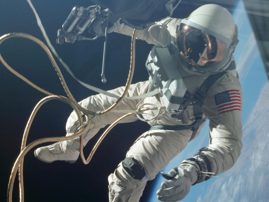An astronaut on a gold tether floating outside his spacecraft, the Earth's edge behind him