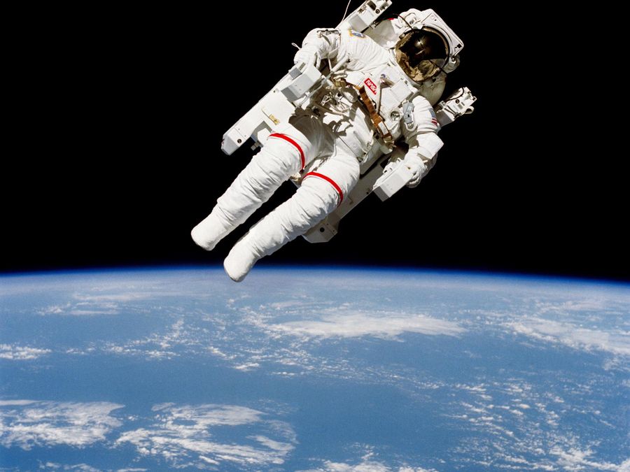 An astronaut in a jet-powered backpack flying free above a blue, cloud-covered Earth